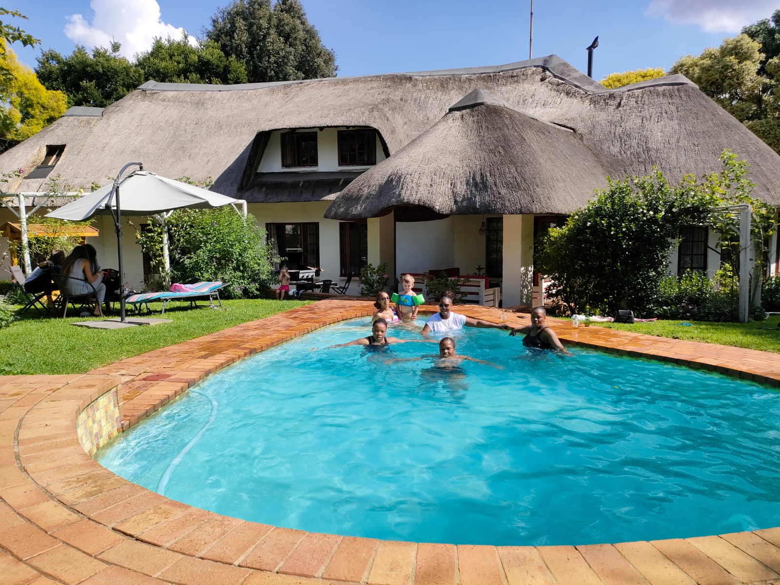 Sunlit pool, deck and thatched lodge in the gardens of a Nelpro property